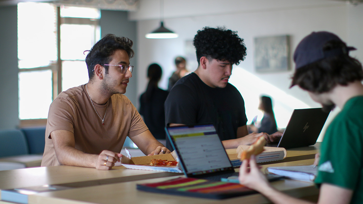 Three students study and eat pizza together at a table