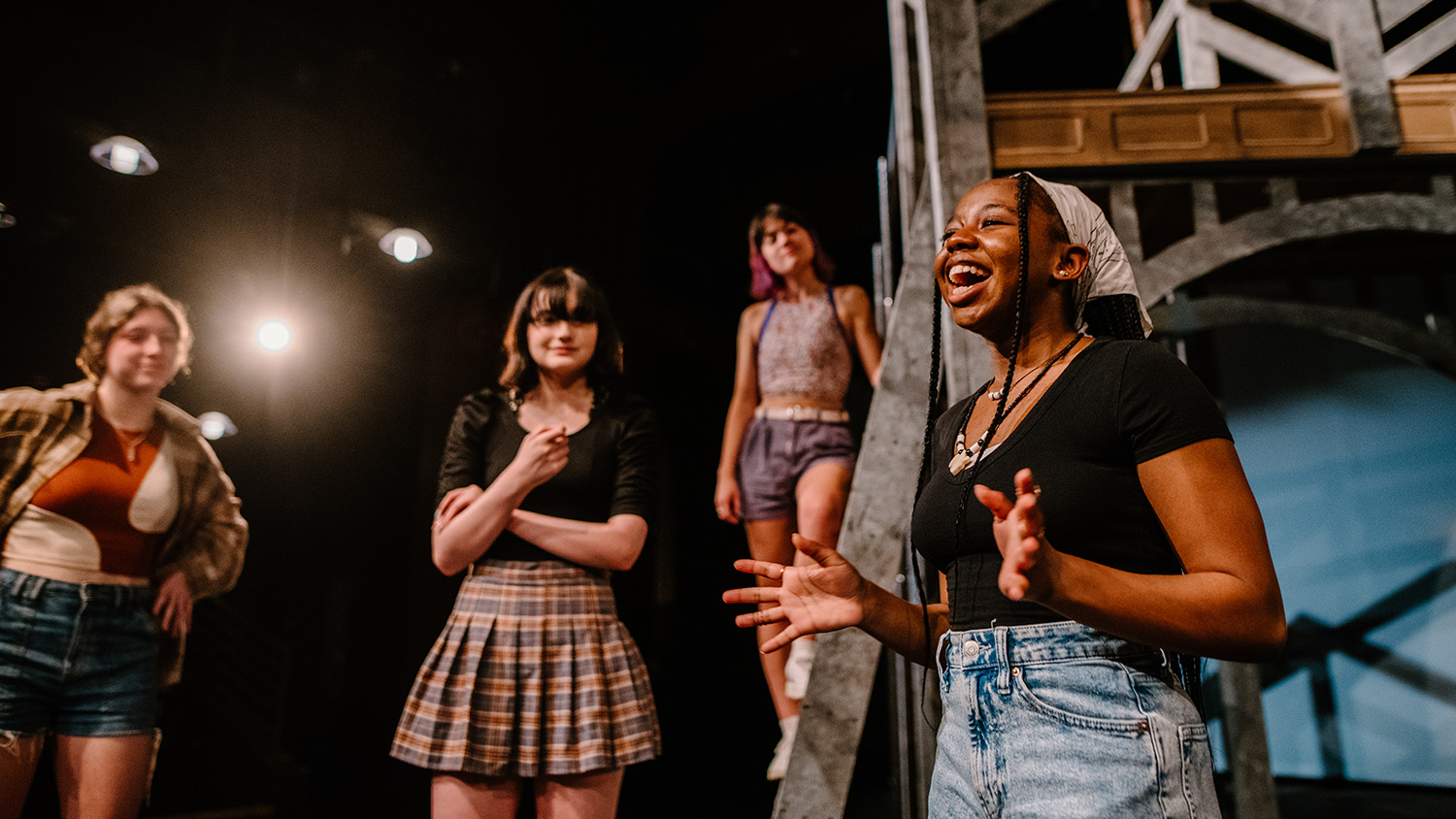 Four students are on a set. One of them is singing on stage.