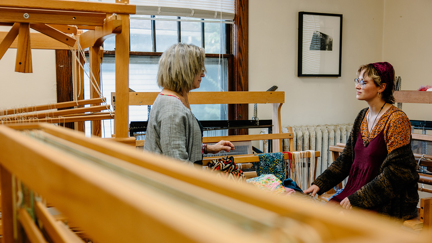 A student talks with an art professor amid weaving looms