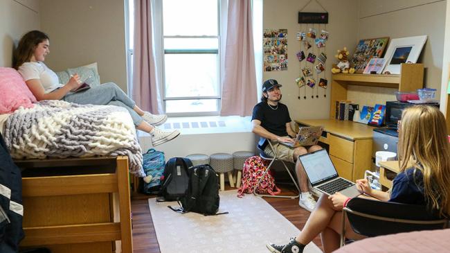 three students socializing in a dorm room