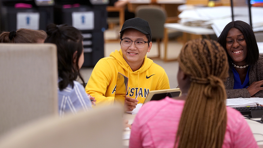 A group of smiling students of various ethnicities studying around a table in Augustana's Thomas Tredway Library