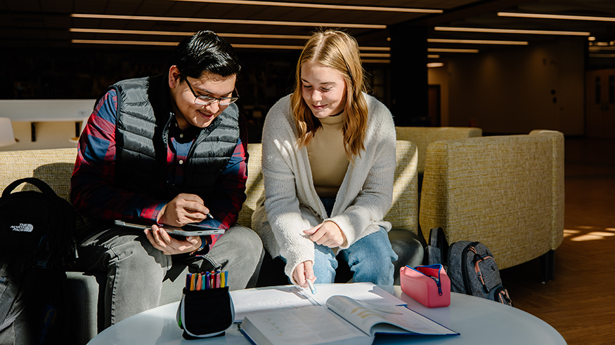 A male and female student studying a textbook using a tablet