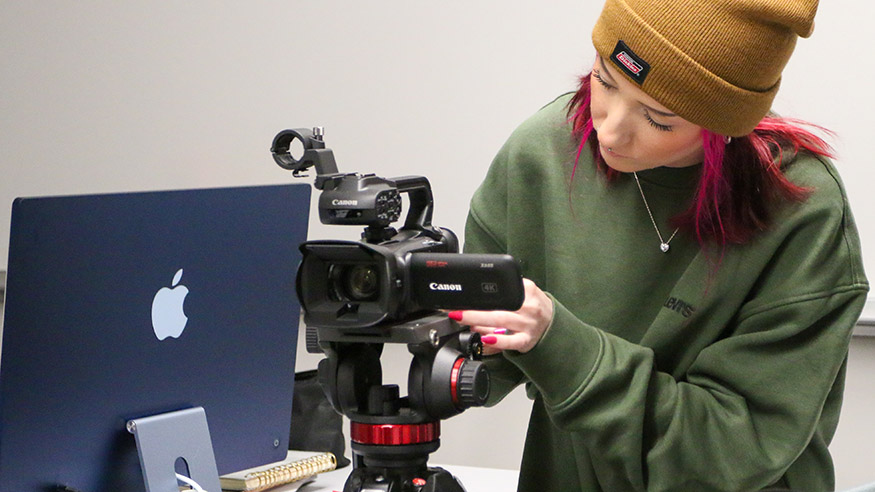 A student wearing a knit cap adjusting the settings on a film camera