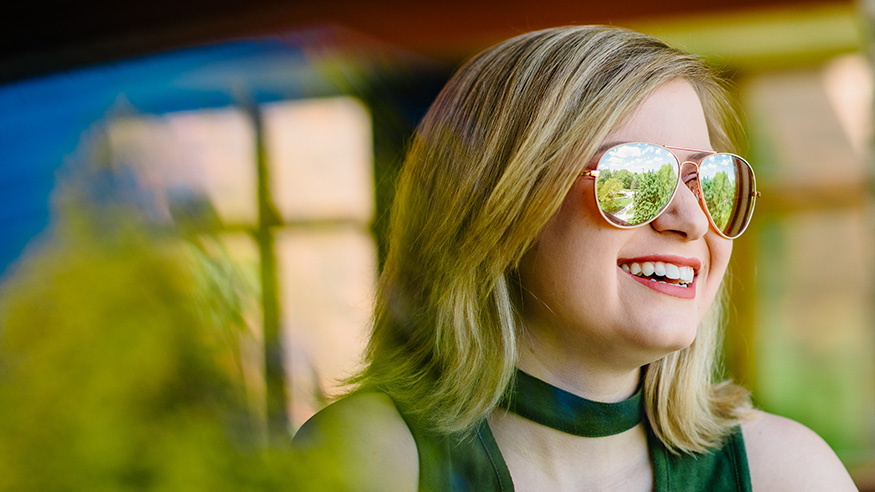 A female student with blond hair looks out the window, with Augustana's campus reflecting in her sunglasses