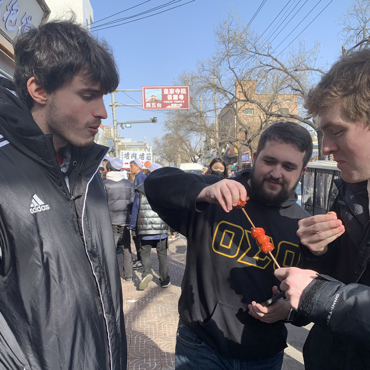 Three male students trying a street snack