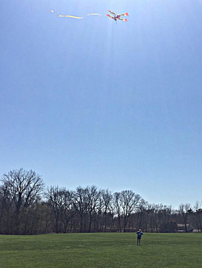 Blue skies and green grass. Paige (girl) flying a kite in the sky.