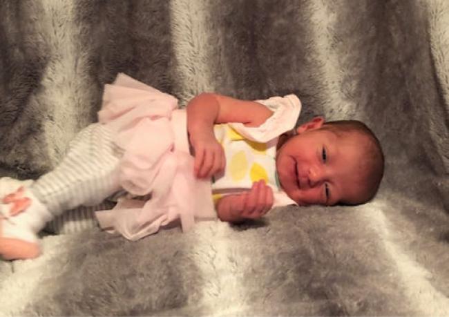 Baby girl in a pink tutu lying on her side with a grey background.