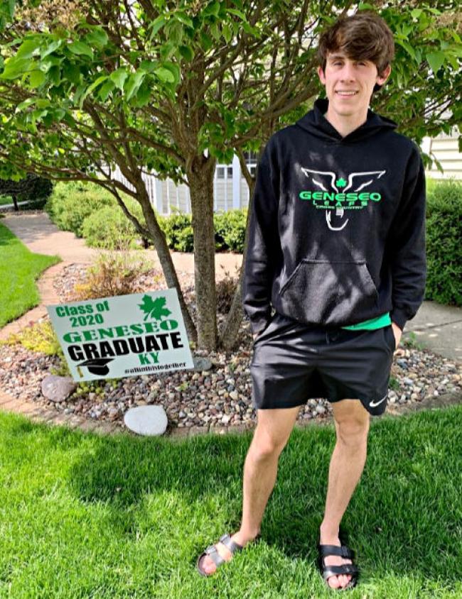 Ky standing to the right of a sign that reads graduating class of 2020 at Geneseo