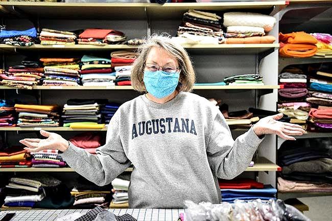 Ellen Dixon surrounded by fabric. Wearing a gray sweatshirt with blue letters on the front that spell Augustana.