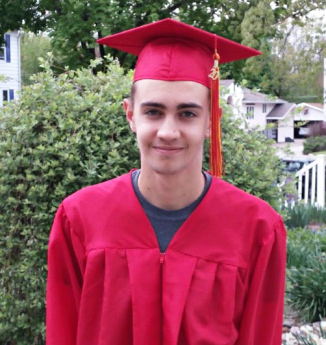 Man in red gown and cap on top of this head. Green tree with leaves in the background.