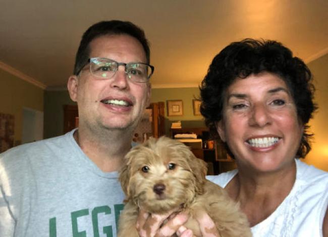 Chris(man) on the right, Laura (woman) on the right and furry, light brown puppy in the middle