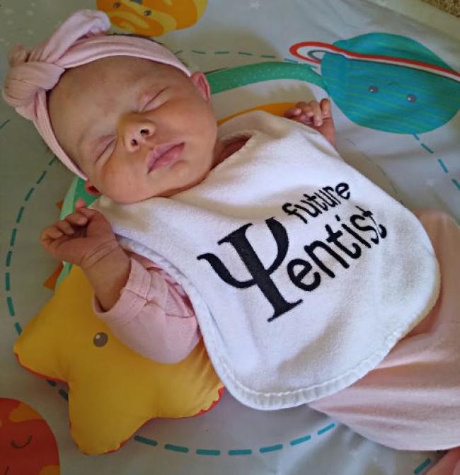 Baby girl Andie, wearing a pink bow and onesie. Her bib says Future Yentist.
