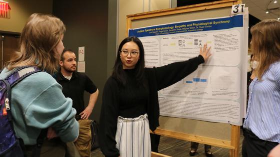 A student presenting a poster to three other students during Celebration of Learning