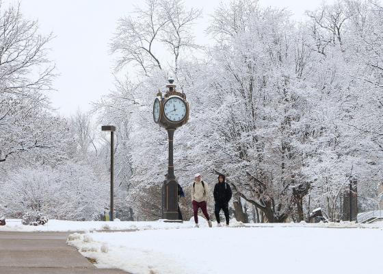 two students walking by a clock on a snowy campus